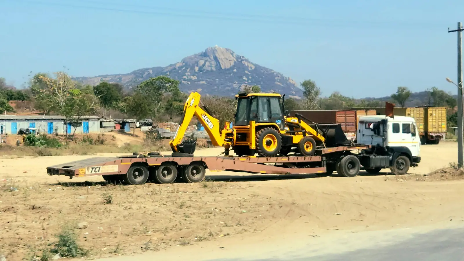 Camión con semirremolque cama baja transportando una retroexcavadora en un camino de zona árida